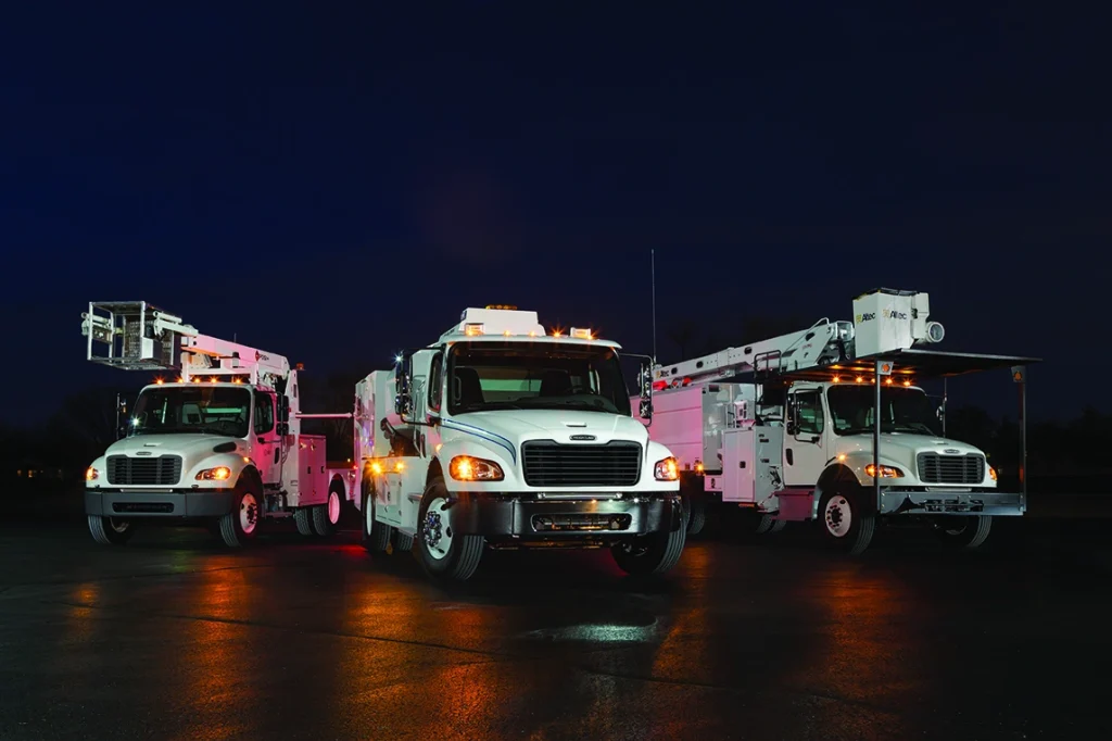 Three white utility trucks at night.